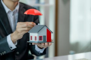 A miniature house with an umbrella, symbolizing the protection offered by Scheduled Property Insurance for valuable assets.